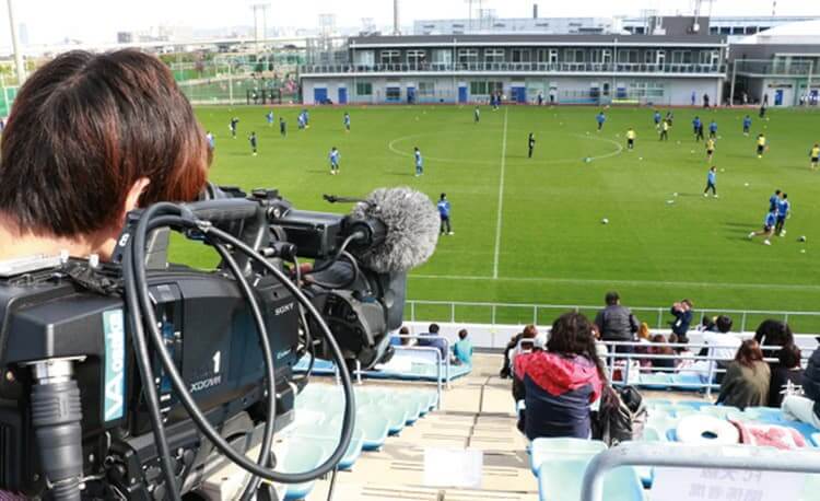 サッカーの試合をコート全体が見える位置から撮影するカメラマン