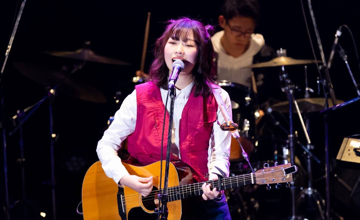 女性シンガーがギター持ち歌唱する様子